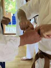Es ist eine Hand zu sehen, Daumen und Zeigefinger berühren sich und bilden einen Kreis. Beide Hände einer zweiten Person versuchen, Zeigefinger und Daumen auseinander zu ziehen.