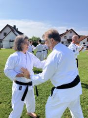 Mehrere Karateka üben auf einer Wiese paarweise. Die Sonne scheint.