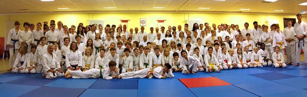 Weit über hundert Karateka sitzen und stehen in einer Halle und schauen in die Kamera. Sämtliche Altersgruppen und Gürtelfarben sind vertreten.